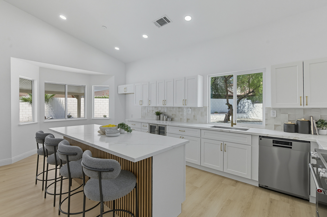 Bright white kitchen with a marble waterfall island, bar seating, and bay windows by Nevada Pro Construction